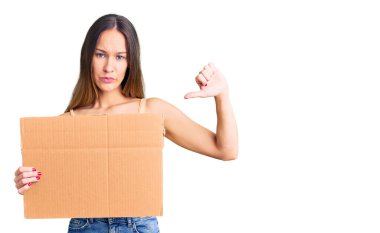 Güzel esmer genç bir kadın elinde karton pankartla boş bir yer, kızgın bir yüz, olumsuz işaret baş parmakları aşağıda, reddedilme konsepti var. 