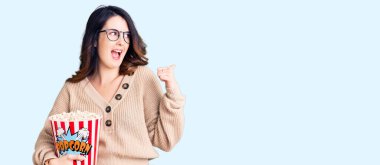 Güzel, genç, esmer bir kadın patlamış mısır yiyor başparmağıyla yan tarafa bakıyor ve ağzı açık gülümsüyor. 