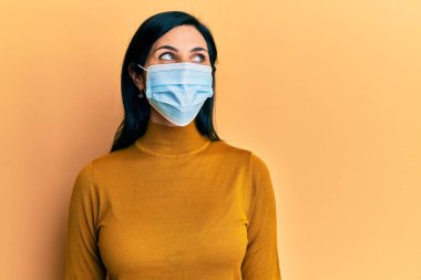 Tıbbi maske takan genç, beyaz bir kadın. Taraf arıyor, profil pozu veriyor. Doğal bir yüzü ve kendine güvenen bir gülümsemesi var.. 