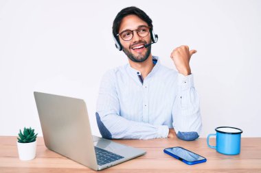 Ofiste çalışan yakışıklı İspanyol bir adam. Operatör kulaklığı takıyor. Başparmağıyla yan tarafa işaret ediyor. 