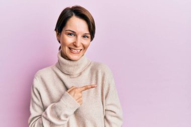 Kısa saçlı, kısa saçlı, neşeli bir süveter giyen, yüzünde mutlu ve doğal bir ifadeyle, elleri ve parmaklarıyla yüzünü gösteren bir gülümseme olan genç esmer kadın. 