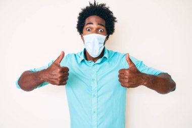 Handsome african american man with afro hair wearing medical mask celebrating crazy and amazed for success with open eyes screaming excited. 