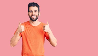 Sakallı, sıradan tişörtler giyen, elinde olumlu jest yapan, gülümseyen ve mutlu genç yakışıklı bir adam. Neşeli ifade ve kazanan jest. 