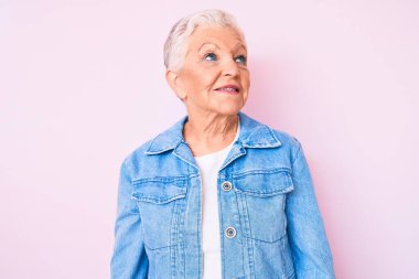 Mavi gözlü, gri saçlı, sıradan kot ceket giyen, yüzünde gülümsemeyle yan yana bakan son sınıf güzeli bir kadın. Kendinden emin gülen. 