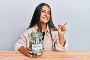 Güzel İspanyol kadın elinde para dolu kavanozla mutlu bir şekilde gülümsüyor. 