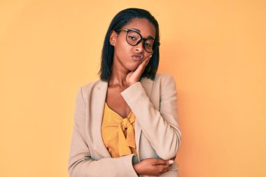 Genç Afro-Amerikalı kadın iş kıyafetleri giyip kollarını kavuşturarak depresyondan sıkılmış ve yorgun göründüğünü düşünüyor.. 