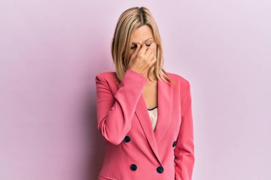 Orta yaşlı beyaz bir kadın iş ceketi giyiyor. Burnu ve gözleri ovuşturmaktan yorulmuş. Yorgunluk ve baş ağrısı çekiyor. Stres ve hüsran kavramı. 