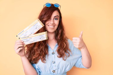 Genç ve güzel bir kadın elinde mutlu ve olumlu bir şekilde gülümseyerek, başparmağını kaldırarak mükemmel ve onay işareti yapıyor. 