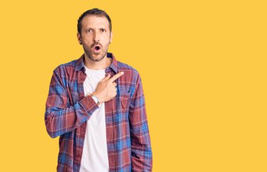 Gündelik giysiler giyen genç yakışıklı adam parmaklarını yana doğru göstererek şaşırdı, ağzı açık hayret içinde kaldı.. 