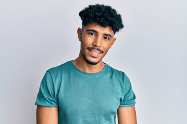 Genç Arap yakışıklı, günlük kıyafetler giyen, pozitif ve mutlu görünen, kendine güvenen, gülümseyen, dişlerini gösteren bir adam. 