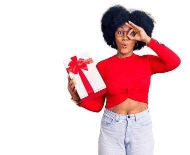 Afro-Amerikalı genç bir kız elinde hediye tutuyor. Şaşırmış bir yüz ve parmaklarından bakan bir gözle iyi bir jest yapıyor. İnançsız ifade. 