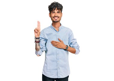 Gündelik kıyafetler giyen genç İspanyol adam gülümsüyor. Göğsü ve parmakları havada küfür ediyor. Sadakat yemini ediyor. 