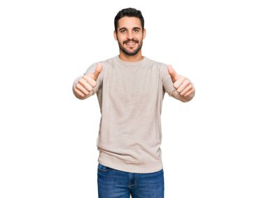 Latin asıllı genç adam gündelik giysiler giyip olumlu jestler yapıyor. Elleriyle gülümsüyor ve başarı için seviniyor. kazanan jest. 