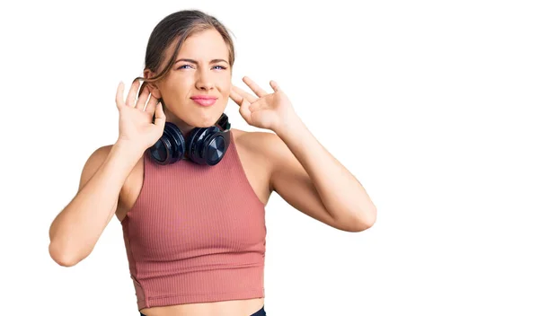 美丽的高加索年轻女子穿着运动服 用耳机试听双手在耳朵上的动作 好奇地闲聊着 听力问题 — 图库照片