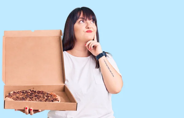 Młody Rozmiar Kobieta Trzymając Pudełko Pizzą Poważna Twarz Myśląc Pytaniu — Zdjęcie stockowe
