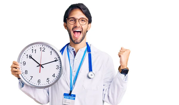 Handsome Hispanic Man Wearing Doctor Uniform Holding Clock Screaming Proud — Stock Photo, Image