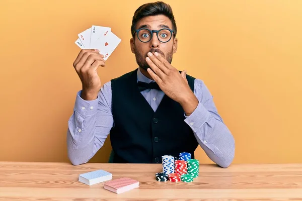 英俊而惊慌失措的男人 手拿着扑克牌和卡片坐在桌子上 惊恐万分 生怕出错 惊讶的表情 — 图库照片