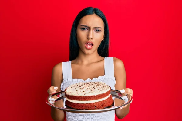 若いですブルネット女性保持ニンジンケーキでショック顔 懐疑的かつ皮肉 驚いていますでオープン口 — ストック写真