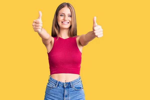 若い美しいブロンドの女性は 手で積極的なジェスチャーを行うことを承認エレガントな夏のシャツを着て 親指を笑顔と成功のために幸せ 勝者のジェスチャー — ストック写真