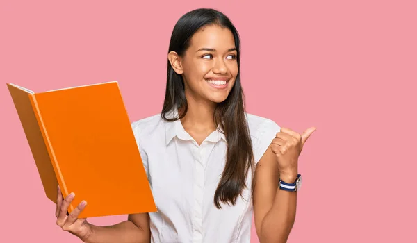 Hermosa Mujer Hispana Leyendo Libro Apuntando Con Pulgar Hacia Costado — Foto de Stock