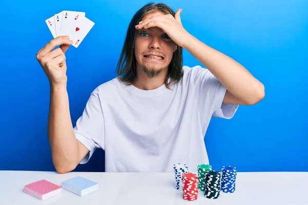英俊的高加索男人 长发打扑克 手里拿着扑克牌 满脸沮丧和沮丧 满脸惊讶和愤怒 — 图库照片