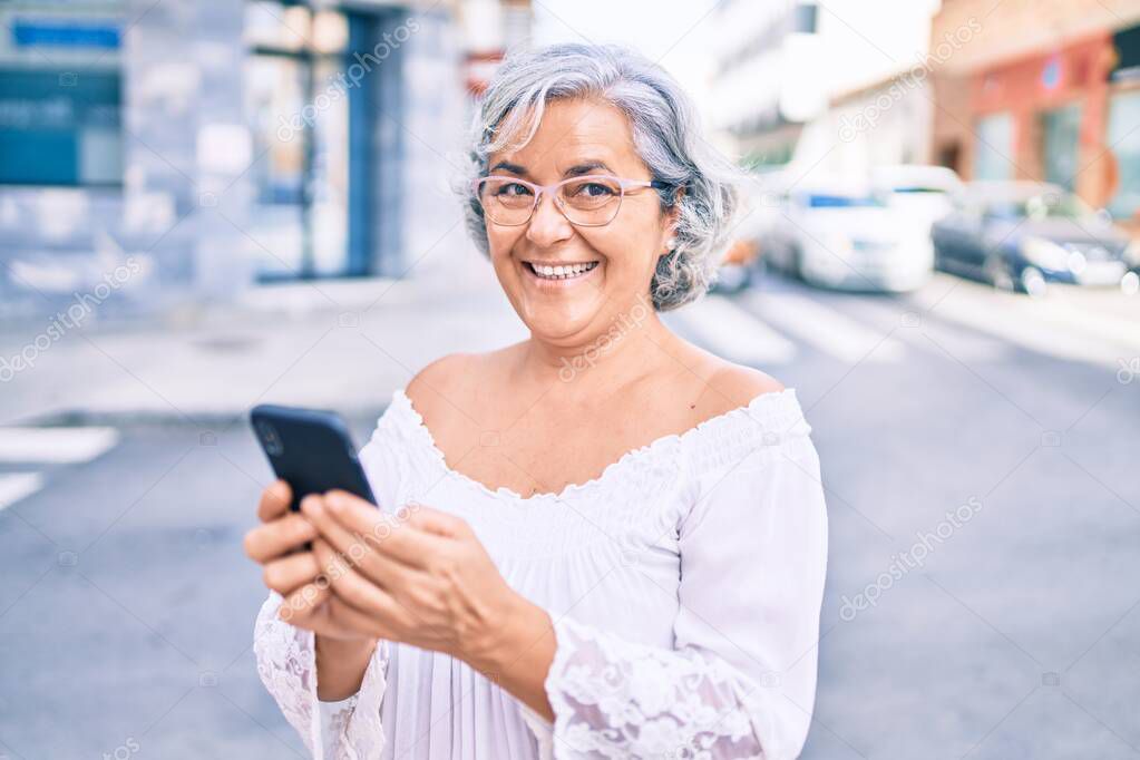 Middle age woman with grey hair smiling happy outdoors using smartphone