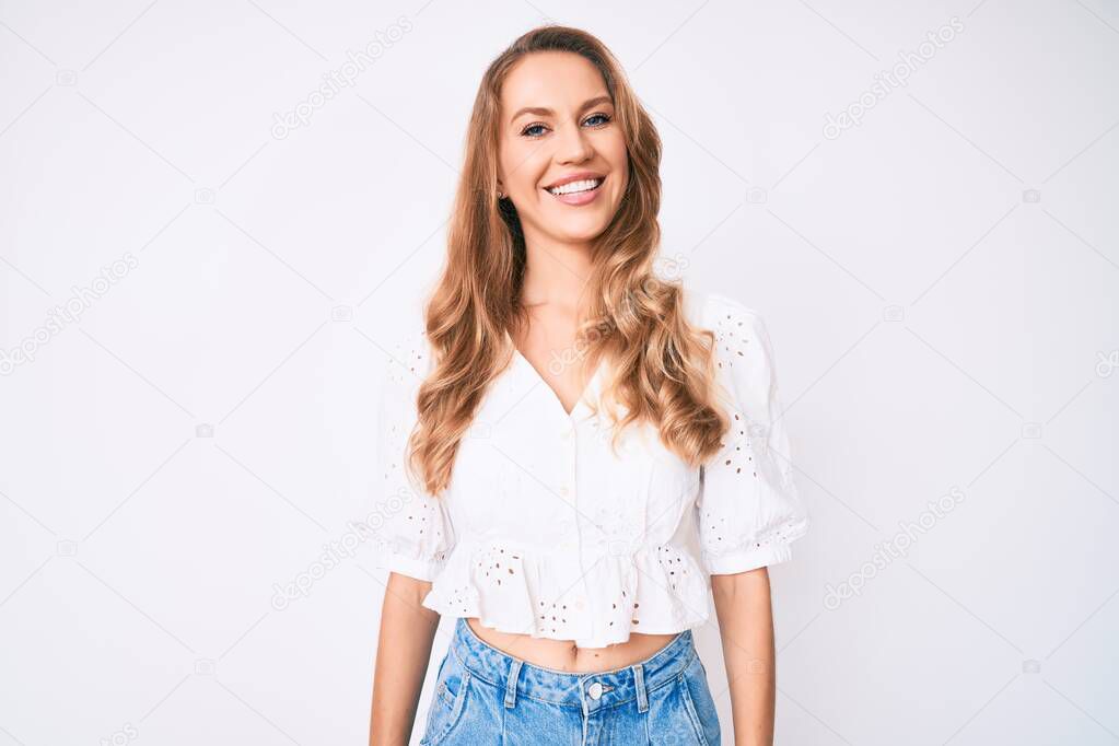 Young caucasian woman with blond hair wearing casual summer clothes looking positive and happy standing and smiling with a confident smile showing teeth 