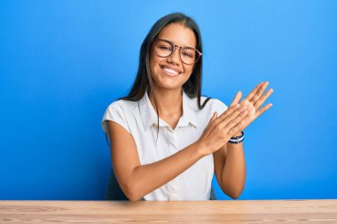 Güzel İspanyol kadın, gündelik giysiler içinde masada oturmuş alkışlıyor ve mutlu ve mutlu, gururlu elleri alkışlıyor. 