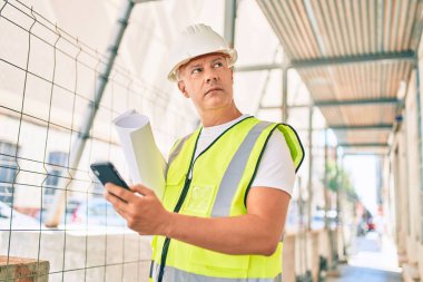 Akıllı telefon kullanan ve şehir planlarını elinde tutan orta yaşlı bir mimar..