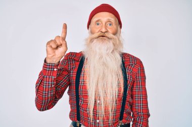 Gri saçlı, uzun sakallı, hippi görünümlü, yün şapkalı yaşlı bir adam bir numaralı parmağını gösterirken kendinden emin ve mutlu bir şekilde gülümsüyor.. 
