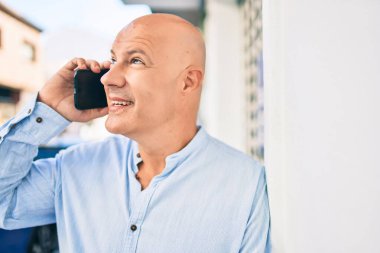 Orta yaşlı kel adam gülümsüyor. Şehirdeki akıllı telefondan mutlu mesut konuşuyor..