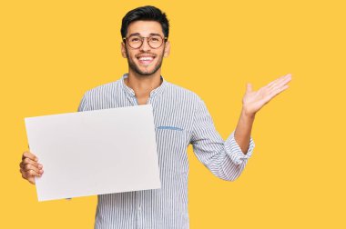 Elinde boş afiş tutan yakışıklı genç adam zaferi mutlu bir gülümsemeyle ve kazanan yüz ifadesiyle kutluyor. 