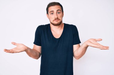 Sıradan kıyafetler giyen, elleri ve kolları havada, kafası karışmış genç ve yakışıklı bir adam. şüphe kavramı. 