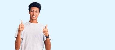 Genç afro-amerikan adam günlük kıyafetler giyiyor başarı işareti yapıyor, elleriyle olumlu jest yapıyor, gülümsüyor ve mutlu. Neşeli ifade ve kazanan jest. 