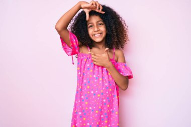 Kıvırcık saçlı, sıradan giyinmiş, gülümseyen, elleri ve parmakları mutlu yüzlü Afro-Amerikan çocuğu. yaratıcılık ve fotoğrafçılık kavramı. 