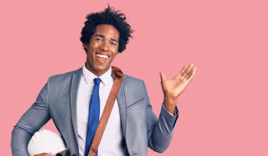 Afro saçlı yakışıklı Amerikalı adam mimar şapkası takıyor zaferi mutlu bir gülümsemeyle kutluyor ve kazanan ifade ellerini kaldırıyor. 