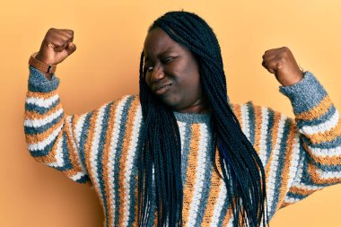 Saçları örgülü genç siyahi bir kadın sıradan bir kazak giyiyor ve gururla gülümsüyor. fitness konsepti. 