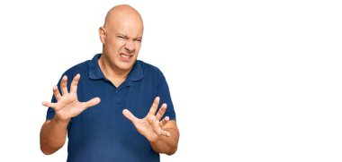 Orta yaşlı, kel, sıradan kıyafetler giyen, tiksindirici, tiksindirici, tiksindirici bir ifade takınan bir adam. Eller havada. 