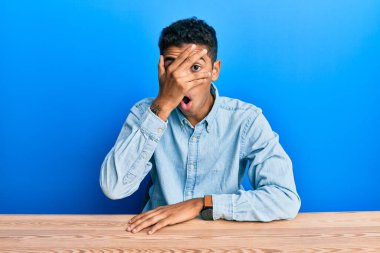 Genç, yakışıklı, Afro-Amerikan bir adam. Günlük giysiler içinde masanın üzerinde oturuyor. Şok olmuş bir şekilde yüzünü ve gözlerini kapıyor.. 