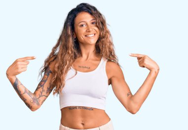 Dövmeli, sıradan kıyafetler giyen, kendine güveni olan, kendini gururlu ve mutlu gösteren genç İspanyol bir kadın.. 