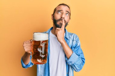 Uzun saçlı ve sakallı çekici bir adam. Yarım litre bira içiyor. Ciddi bir yüz ifadesi var. 