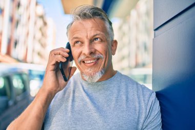 Orta yaşlı, İspanyol, gri saçlı, gülümseyen, mutlu, akıllı telefondan konuşan bir adam..