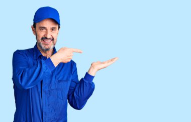 Orta yaşlı, tamirci üniforması giyen yakışıklı adam kameraya hayret ediyor ve gülümsüyor.. 