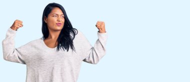 Uzun saçlı, sıradan kıyafetler giyen İspanyol kadın gururla gülümseyen kol kaslarını gösteriyor. fitness konsepti. 