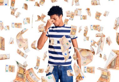 Genç Afro-Amerikan adam günlük kıyafetler giyip yorgun burnu ve gözleri ovuşturup yorgun ve baş ağrısı çekiyor. Stres ve hüsran kavramı.