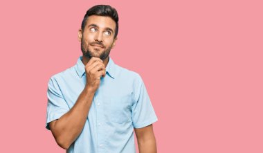 Elleri çenesinde gündelik kıyafetler giyen yakışıklı İspanyol bir adam soru soruyor, düşünceli bir yüz ifadesi var. Düşünceli bir yüzle gülümsüyor. şüphe kavramı. 