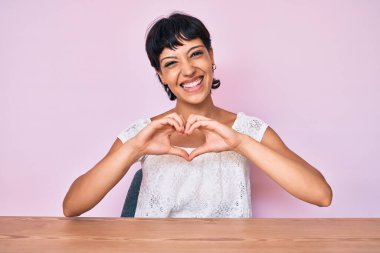 Güzel esmer kadın, pembe arka plan üzerine günlük kıyafetler giyip, sevgiyle gülümsüyor. Elleriyle kalp sembolü ve şekli gösteriyor. romantik kavram. 