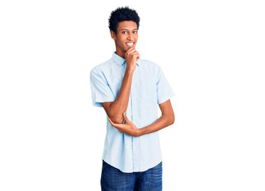 Sıradan kıyafetler giyen genç Afro-Amerikalı adam kameraya kendinden emin bakıyor kollarını kavuşturmuş ve çenesini kaldırmış gülümsüyor. Olumlu düşünmek. 