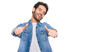 Latin asıllı genç adam gündelik giysiler giyip olumlu jestler yapıyor. Elleriyle gülümsüyor ve başarı için seviniyor. kazanan jest. 