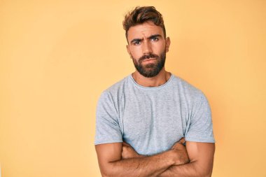 Gündelik kıyafetler giyen, kuşkucu ve gergin genç İspanyol bir adam. Yüzünde çapraz kollarla onaylamayan bir ifade var. negatif kişi. 